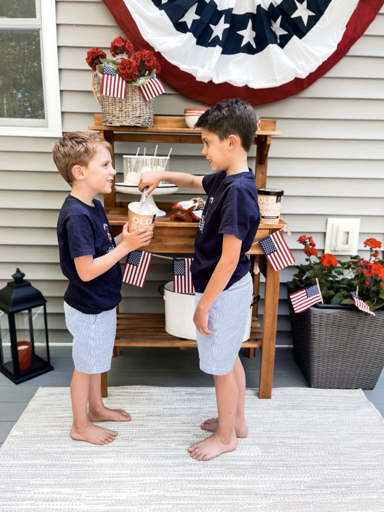 Two young boys in navy t-shirts in front of 4th of July red white and blue decorated table with root beer floats in hand