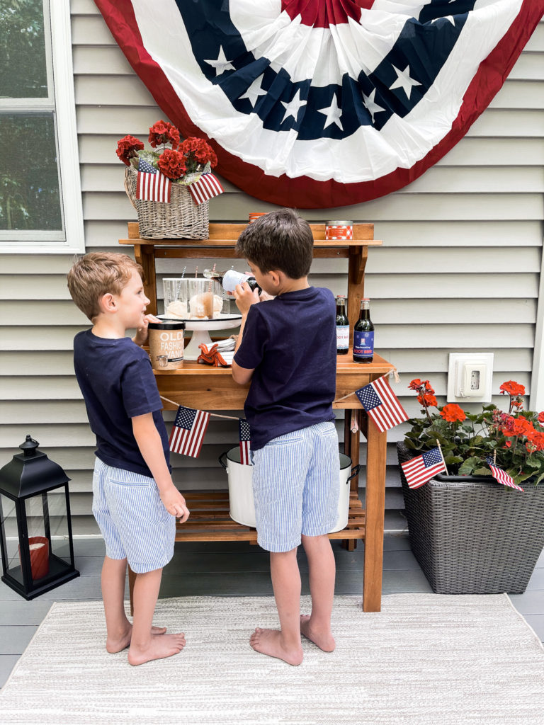 Two young boys in navy t-shirts in front of 4th of July red white and blue decorated table with root beer floats in hand