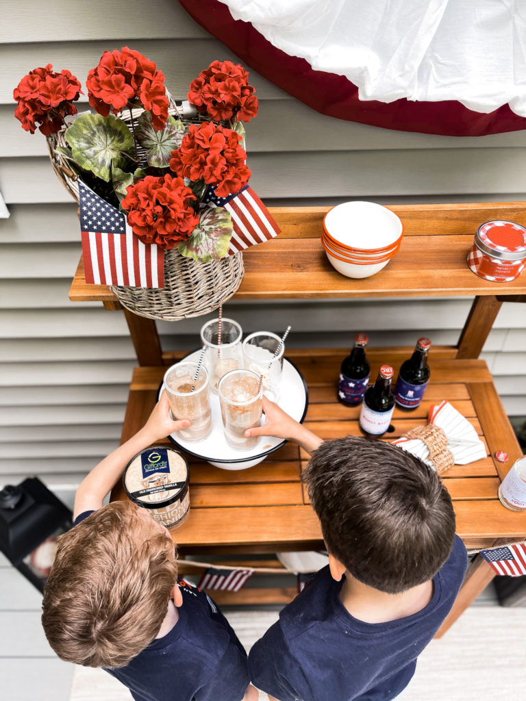 Two young boys in navy t-shirts in front of 4th of July red white and blue decorated table with root beer floats in hand