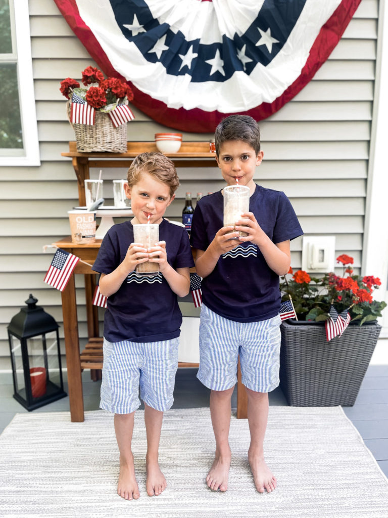 Two young boys in navy t-shirts in front of 4th of July red white and blue decorated table with root beer floats in hand